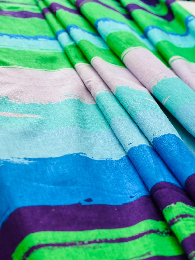 May include: Striped fabric with a colorful abstract design. The fabric features alternating stripes of green, purple, blue, and light blue. The stripes are painted with a brushstroke effect.