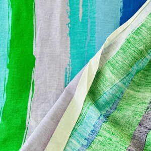 May include: Close-up of a fabric with a striped pattern. The fabric is a mix of green, blue, and white stripes. The stripes are painted on the fabric and have a brushstroke effect.