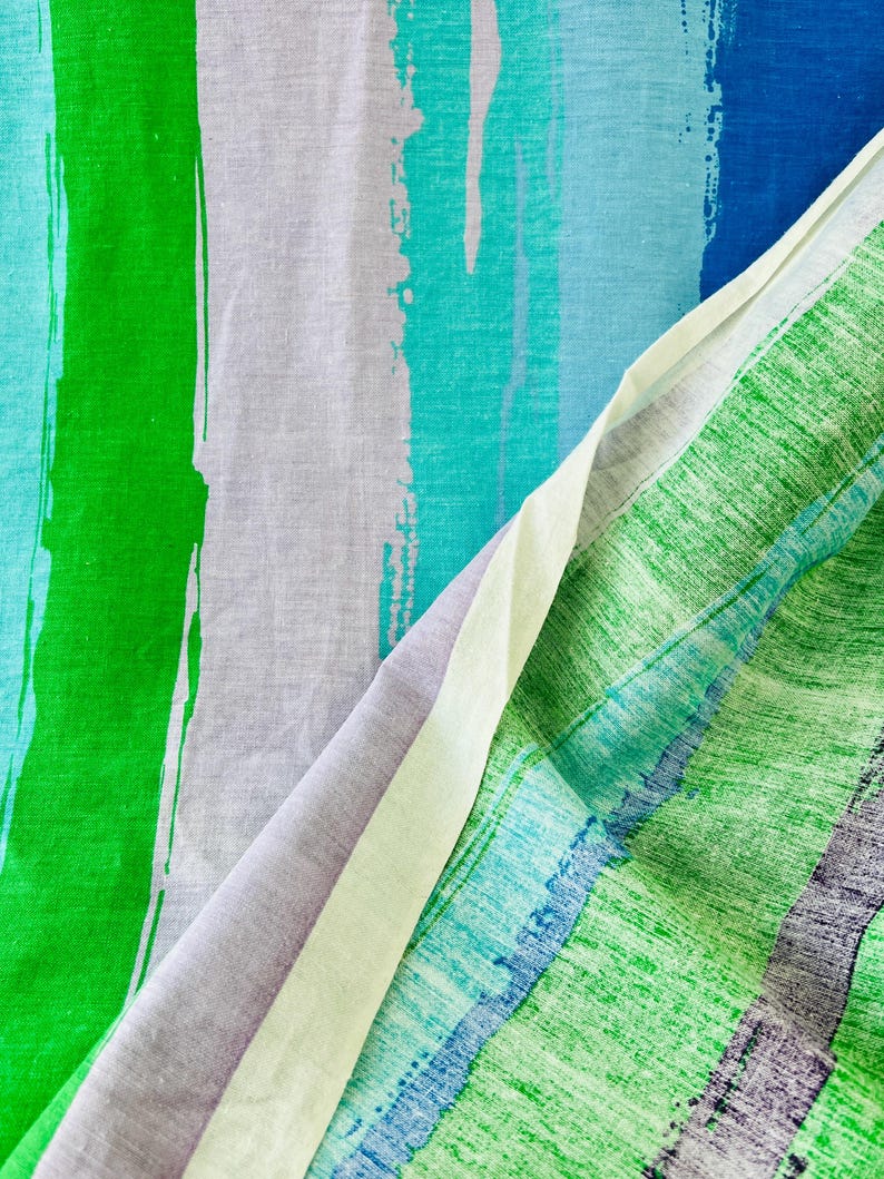 May include: Close-up of a fabric with a striped pattern. The fabric is a mix of green, blue, and white stripes. The stripes are painted on the fabric and have a brushstroke effect.