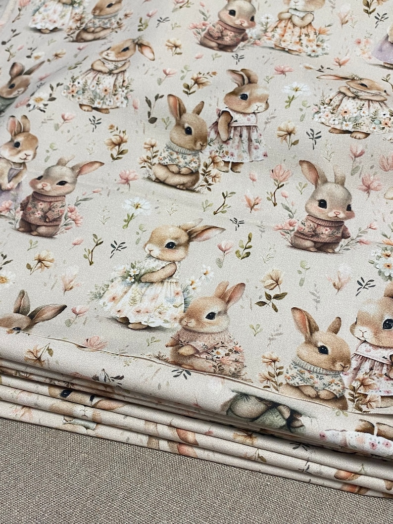May include: Beige fabric with a repeating pattern of brown bunnies wearing different outfits and holding flowers. The bunnies are surrounded by small green leaves and white flowers.