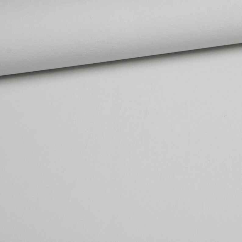 Puede incluir: Una tela de color gris claro s&oacute;lido con una textura suave y uniforme. El material est&aacute; doblado en el borde superior, creando una l&iacute;nea de sombra suave que resalta el acabado mate y el color constante de la superficie textil en la imagen.