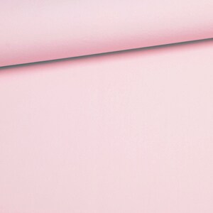 May include: A close-up of a roll of light pink fabric. The fabric is smooth and appears to be a solid color. The top edge of the fabric is rolled over, creating a slight shadow.