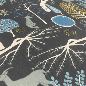May include: A dark gray fabric with a repeating pattern of stylized trees, deer, and other woodland creatures in shades of blue, white, and yellow.