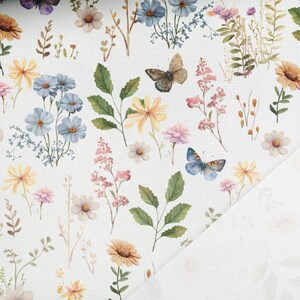 May include: A white fabric with a repeating pattern of blue and yellow flowers, green leaves, and butterflies. The fabric has a subtle texture.