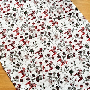 Könnte beinhalten: Weißer Stoff mit einem sich wiederholenden Muster aus roten und grauen stilisierten Pferden und floralen Designs.