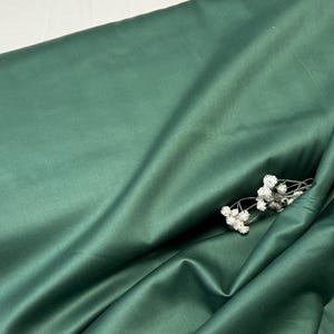 Könnte beinhalten: Ein glatter, tiefgrüner Stoff mit einem dezenten Glanz. Der Stoff ist gefaltet und drapiert und erzeugt weiche Falten und Kurven.