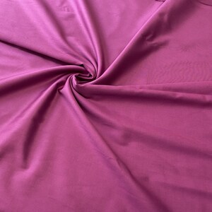 May include: A close-up shot of a vibrant magenta fabric, artfully draped and swirled to create a dynamic texture. The fabric's smooth surface reflects light, highlighting its rich color and subtle sheen. Ideal for apparel or home decor.