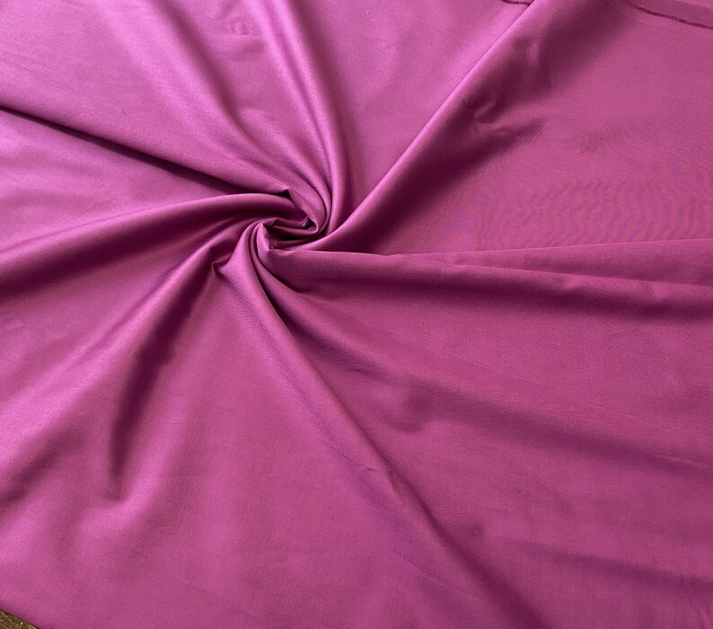 May include: A close-up shot of a vibrant magenta fabric, artfully draped and swirled to create a dynamic texture. The fabric's smooth surface reflects light, highlighting its rich color and subtle sheen. Ideal for apparel or home decor.