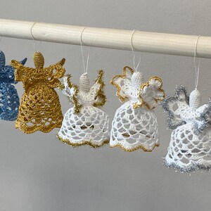 May include: Five crocheted angel ornaments hanging from a white rod. The angels are white with gold and silver trim. One angel is blue with silver trim.