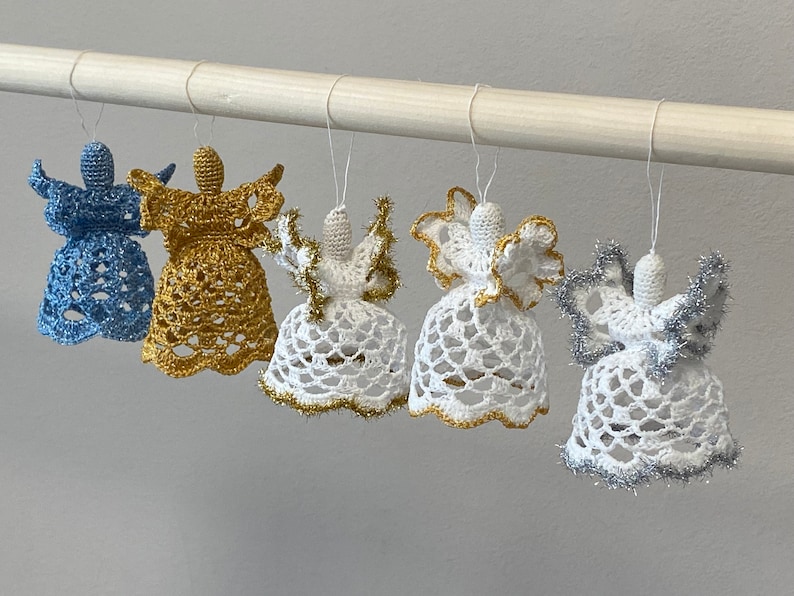 May include: Five crocheted angel ornaments hanging from a white rod. The angels are white with gold and silver trim. One angel is blue with silver trim.