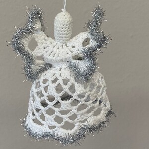 May include: White crocheted angel ornament with silver tinsel trim. The angel has a bell-shaped skirt and a halo.