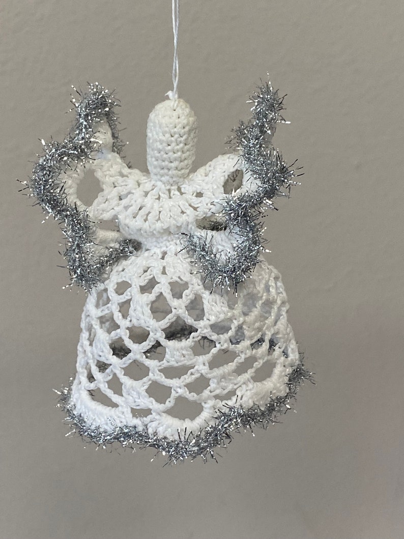 May include: White crocheted angel ornament with silver tinsel trim. The angel has a bell-shaped skirt and a halo.