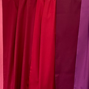 May include: A collection of draped fabric in shades of red and purple. The colors range from light pink to deep burgundy and violet. The fabric is smooth and appears to be a lightweight material.