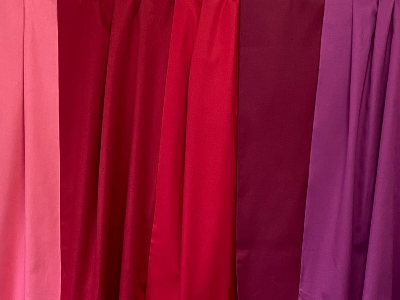 May include: A collection of draped fabric in shades of red and purple. The colors range from light pink to deep burgundy and violet. The fabric is smooth and appears to be a lightweight material.