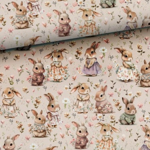May include: A beige fabric with a repeating pattern of bunnies wearing different outfits and holding flowers. The bunnies are surrounded by pink and white flowers and green leaves.