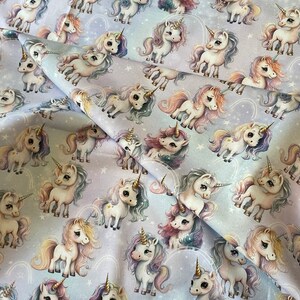 May include: A white fabric with a repeating pattern of colorful unicorns with rainbow horns and manes. The unicorns are standing on a light purple background with white stars.