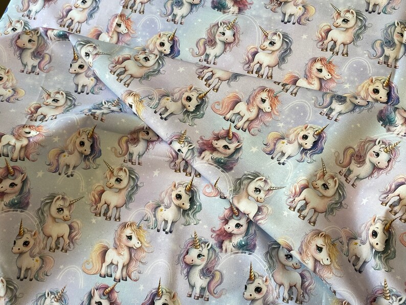 May include: A white fabric with a repeating pattern of colorful unicorns with rainbow horns and manes. The unicorns are standing on a light purple background with white stars.