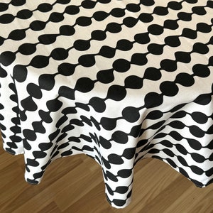 Op de afbeelding: Ronde zwarte en witte tafelkleed met een herhalend patroon van abstracte vormen. Het tafelkleed is gemaakt van stof en heeft een gladde textuur.