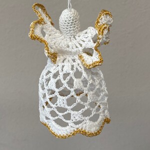 May include: White crocheted angel ornament with gold trim. The angel has a bell-shaped body and outstretched wings.