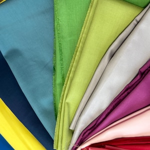 May include: A fan of colorful fabric swatches in shades of yellow, blue, teal, green, silver, purple, and pink. The fabric appears to be a smooth, possibly silk or satin material, with a slight sheen. The arrangement showcases a variety of colors.