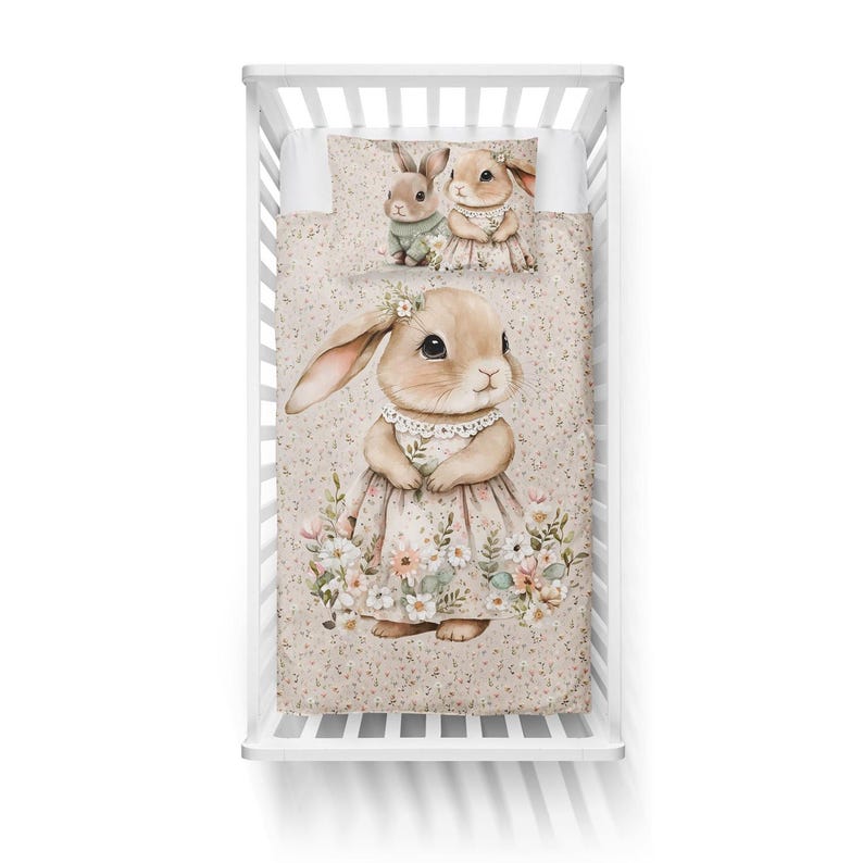 May include: A crib set featuring a watercolor illustration of bunnies. The set includes a fitted sheet, a pillowcase, and a quilt. The quilt and pillowcase have a repeating pattern of small flowers. The main bunny wears a floral dress.