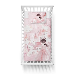 May include: A pink and white crib bedding set with a unicorn and princess theme. The bedding features a pink castle, clouds, and stars. The pillowcase has a princess with brown hair and a pink dress.