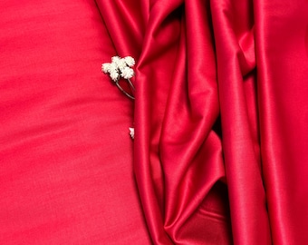 May include: A close-up of a deep red satin fabric with a few white flowers tucked into a fold.