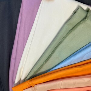 May include: A collection of folded fabric in various colors, including black, lavender, white, green, light blue, orange, and peach. The fabrics are arranged in a fan-like pattern, showcasing the different hues and textures.