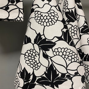 May include: Three black and white kitchen towels with a floral pattern. The towels are hanging on a hook.