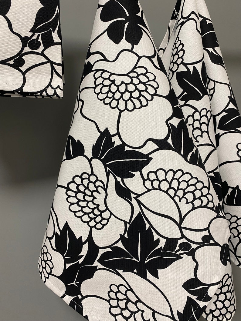 May include: Three black and white kitchen towels with a floral pattern. The towels are hanging on a hook.