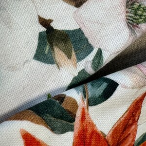 May include: Close-up of a fabric with a floral print. The fabric features a white background with red, green, and pink flowers. The flowers are detailed and realistic.