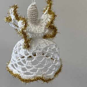 May include: White crocheted angel ornament with gold tinsel trim. The angel has a bell-shaped skirt and a small head with a halo.
