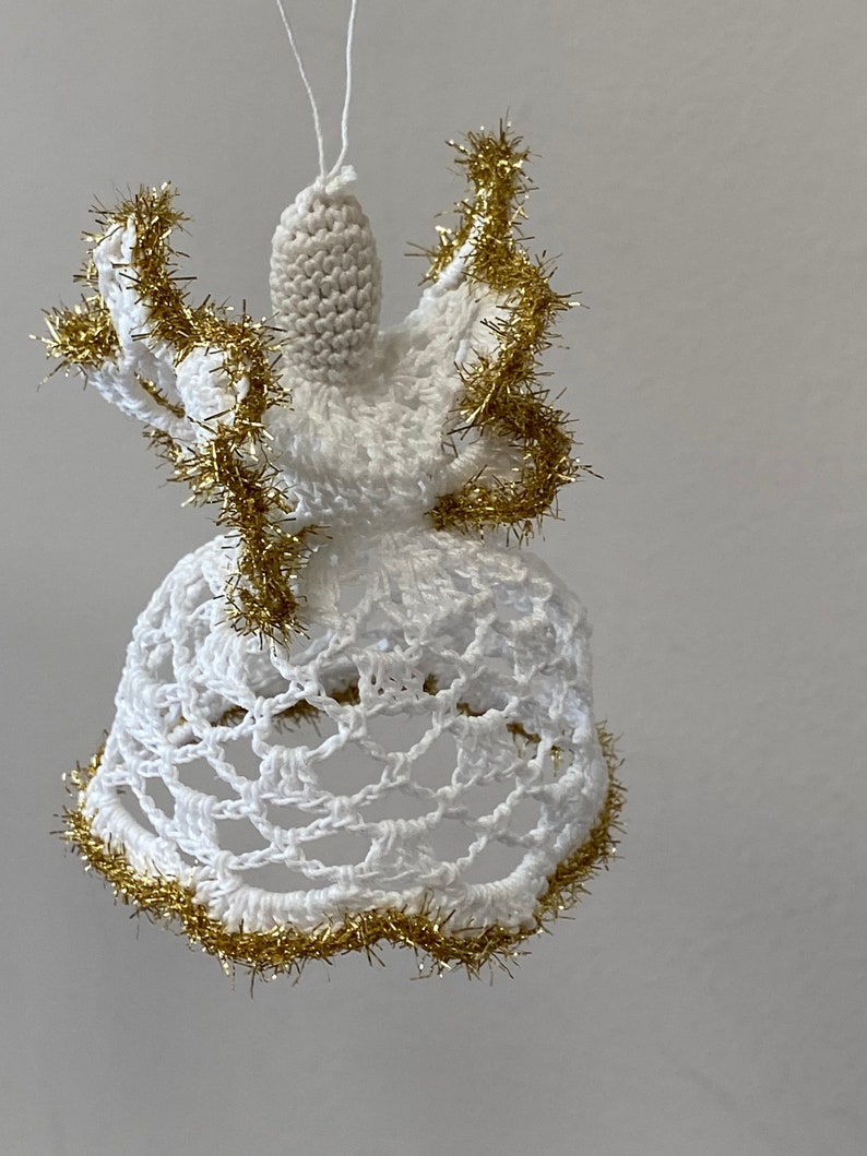 May include: White crocheted angel ornament with gold tinsel trim. The angel has a bell-shaped skirt and a small head with a halo.
