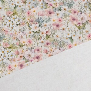 May include: A white fabric with a floral pattern featuring pink, white, and green flowers. The fabric has a soft, textured feel.