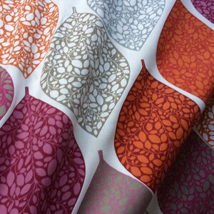 May include: A white fabric with a repeating pattern of stylized leaves in shades of orange, pink, and gray. The leaves are filled with smaller, irregular shapes.