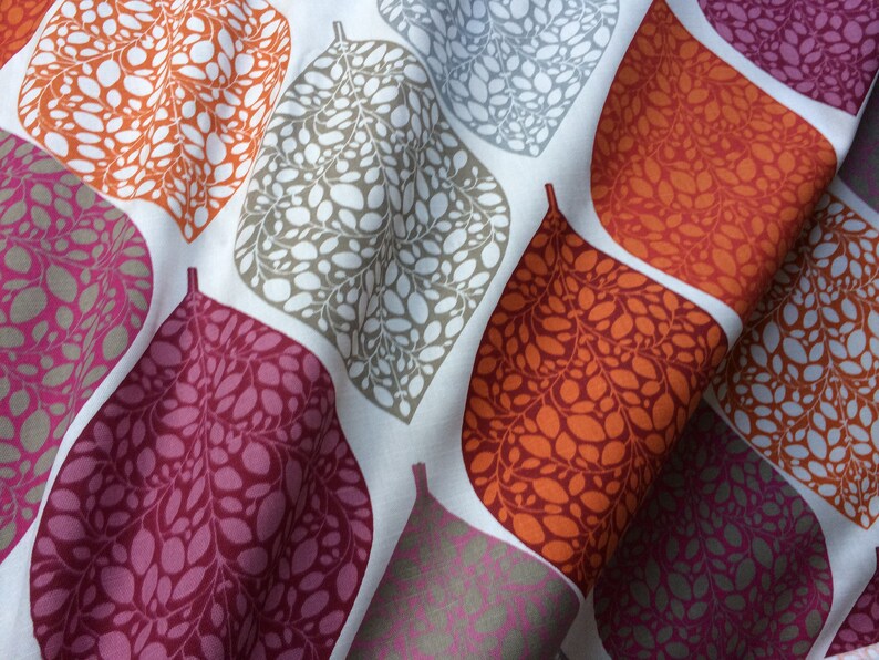 May include: A white fabric with a repeating pattern of stylized leaves in shades of orange, pink, and gray. The leaves are filled with smaller, irregular shapes.