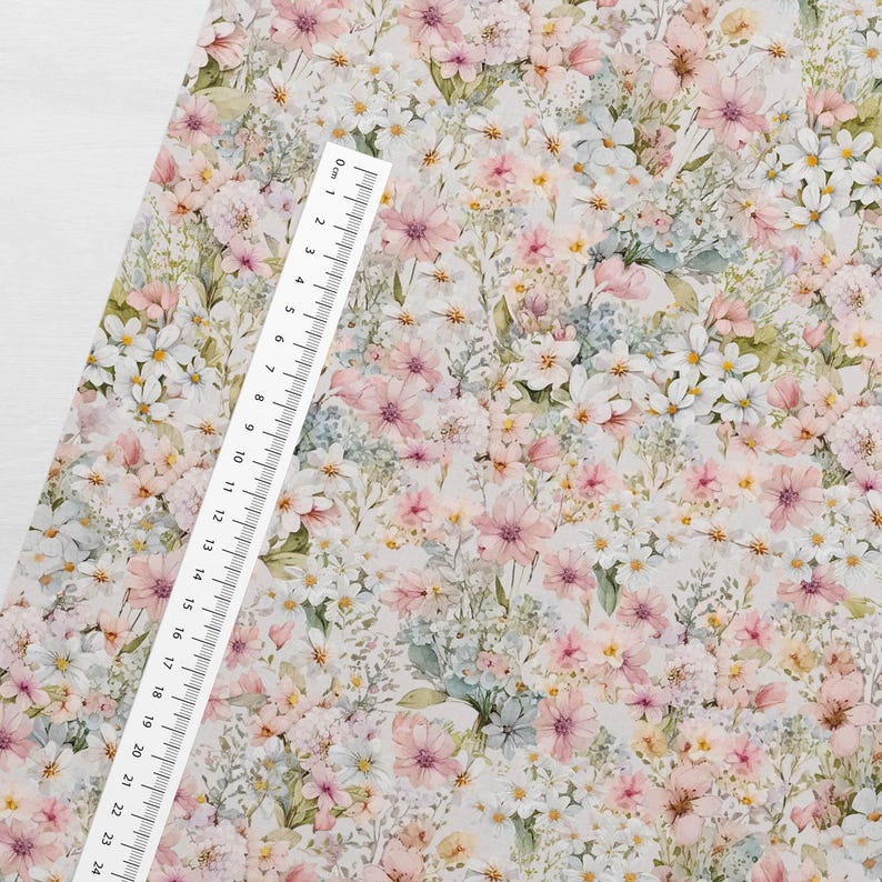 May include: A white fabric with a floral pattern featuring pink, white, and blue flowers. The fabric has a watercolor effect and is perfect for crafting projects.