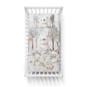 Puede incluir: Un juego de ropa de cama de cuna blanca con un tema de bosque. La ropa de cama presenta un fondo blanco con &aacute;rboles marrones, un oso blanco, un conejo, un rat&oacute;n y patitos. La ropa de cama est&aacute; hecha de tela suave y c&oacute;moda.