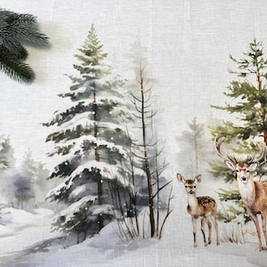 Op de afbeelding: Textiel met een winterlandschap, geschilderd met aquarelverf, met een besneeuwd bos, groenblijvende bomen en twee herten. De herten zijn bruin met witte vlekken. Een tak van een naaldboom staat linksboven.