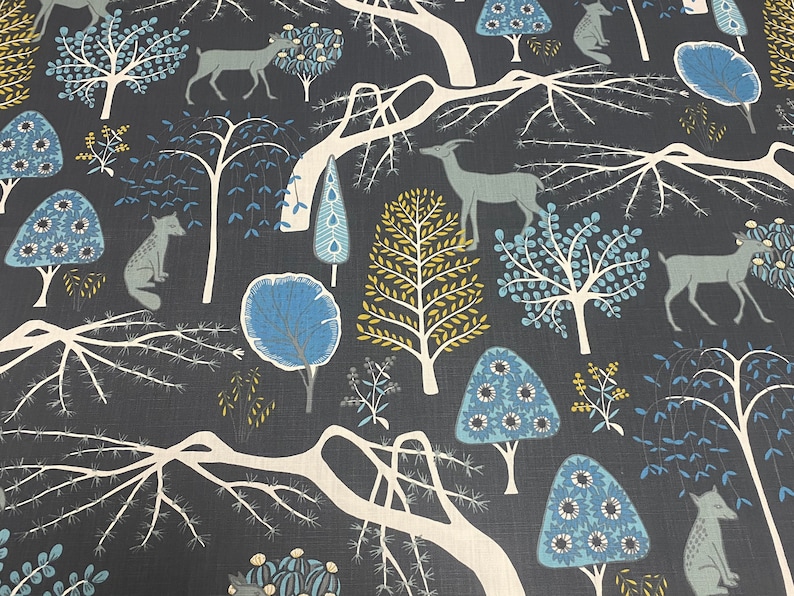May include: A dark blue fabric with a repeating pattern of stylized trees, deer, and foxes. The trees have blue and yellow leaves. The deer and foxes are white.