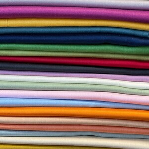May include: A stack of folded fabric in various colors, including yellow, purple, pink, teal, green, red, and blue. The fabric appears to be a smooth, solid material, possibly cotton or silk, suitable for sewing or crafting projects.