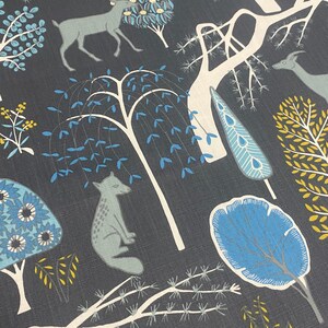 May include: A dark blue fabric with a repeating pattern of stylized trees, deer, and foxes. The trees are white with blue and yellow leaves. The deer and foxes are gray. The background is a dark blue.