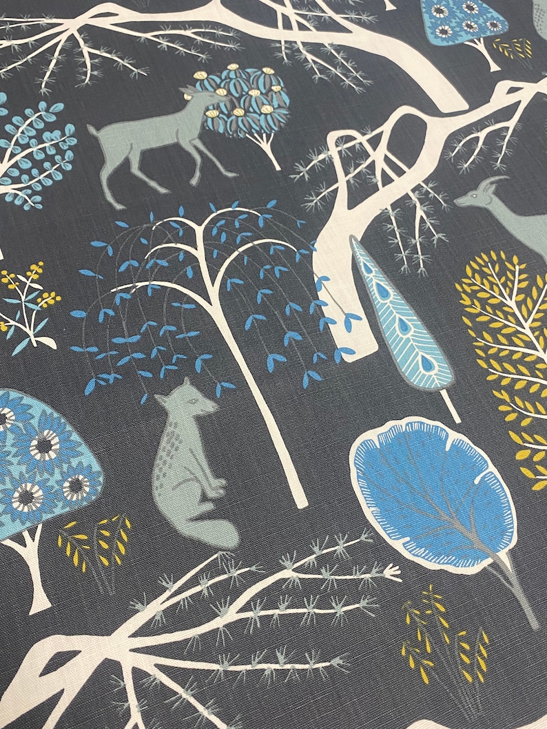 May include: A dark blue fabric with a repeating pattern of stylized trees, deer, and foxes. The trees are white with blue and yellow leaves. The deer and foxes are gray. The background is a dark blue.
