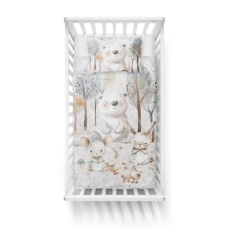 May include: A white crib bedding set with a woodland theme. The bedding features a white background with brown trees, a white bear, a rabbit, a mouse, and ducks. The bedding is made of soft, comfortable fabric.