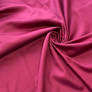 May include: Close-up of a swirl of deep magenta fabric. The material has a smooth, silky texture with subtle highlights and shadows. The fabric is gathered in the center, creating a spiral effect.