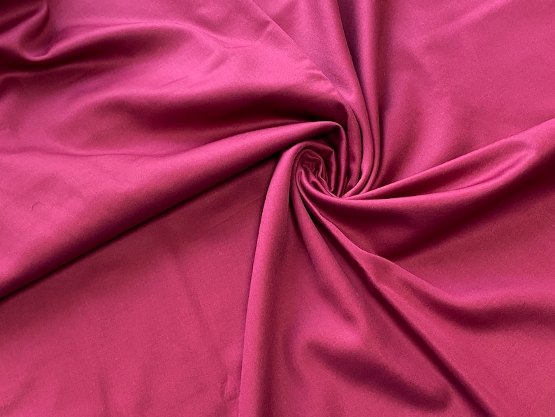 May include: Close-up of a swirl of deep magenta fabric. The material has a smooth, silky texture with subtle highlights and shadows. The fabric is gathered in the center, creating a spiral effect.