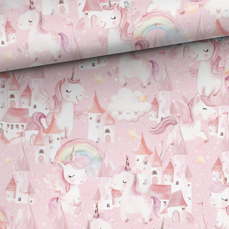 May include: Pink fabric featuring a repeating pattern of unicorns, castles, rainbows, and clouds. The unicorns have pink manes and wings. The castles have pink and orange turrets. The background is a light pink color with small white speckles.