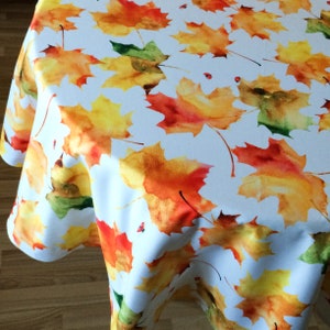 Peut inclure: Nappe blanche avec un motif aquarelle de feuilles orange, jaunes et vertes. Les feuilles sont éparpillées sur la nappe et ont un aspect réaliste.