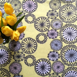 May include: A yellow tablecloth with a repeating pattern of black and white circles with a radiating design. A bouquet of yellow tulips is in the center of the tablecloth.