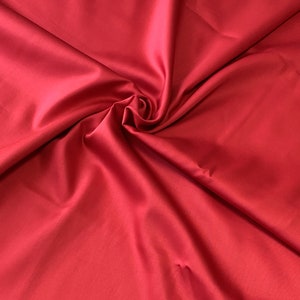 May include: A close-up shot of a vibrant red fabric with a smooth, satin-like texture. The fabric is gathered and swirled, creating soft folds and shadows. The color is a rich, solid red, with a slight sheen.